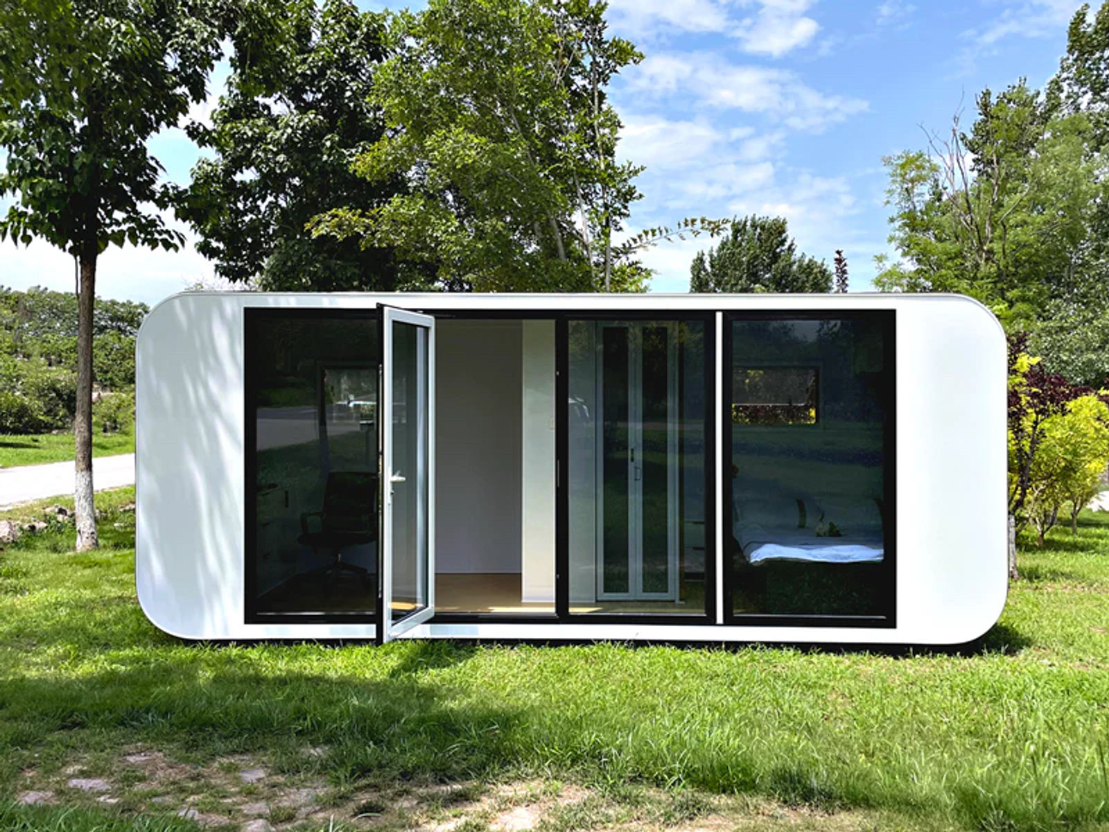 Apple Cabin set on a lawn among trees with its front door open, the desk and bed visible through the full-height glass wall